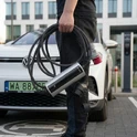 rzenośna ładowarka BN70 w użyciu - ładowanie przy samochodzie elektrycznym VW Mężczyzna trzymający przenośną ładowarkę Besen BN70 przed samochodem elektrycznym Volkswagen na parkingu w Warszawie